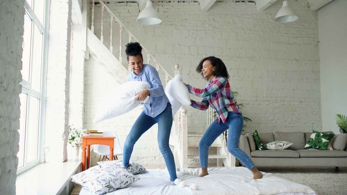 Mixed race young pretty girls jumping on bed and fight pillows having fun related to Battle Bed Bugs with Home Depot: Top Sprays for a Sound Sleep