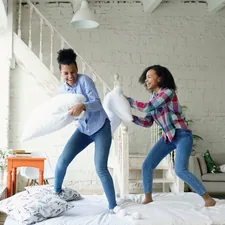 Mixed race young pretty girls jumping on bed and fight pillows having fun related to Battle Bed Bugs with Home Depot: Top Sprays for a Sound Sleep