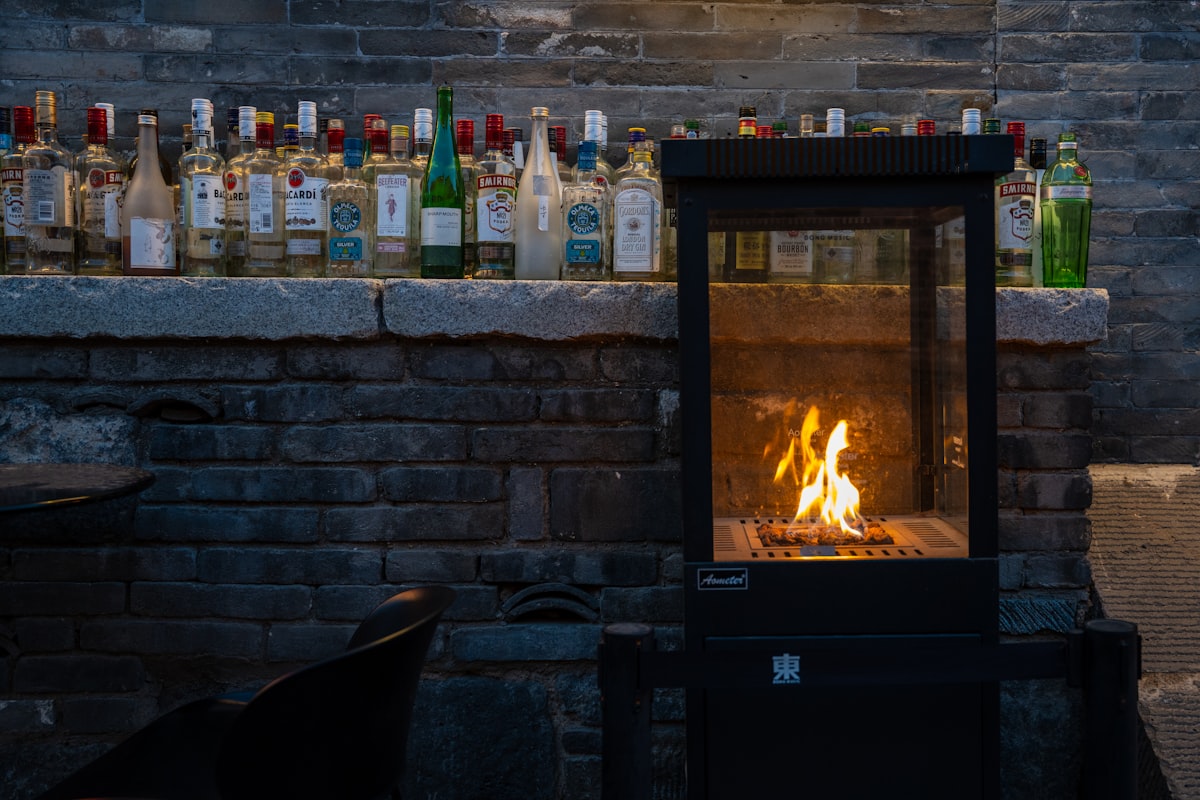 Modern fireplace with flames and bottles on a stone ledge. related to Embracing the Heat: Large Cast Iron Chimineas for Your Outdoor Space