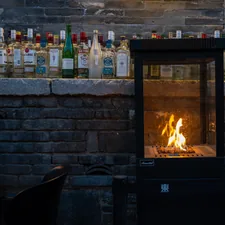 Modern fireplace with flames and bottles on a stone ledge. related to Embracing the Heat: Large Cast Iron Chimineas for Your Outdoor Space
