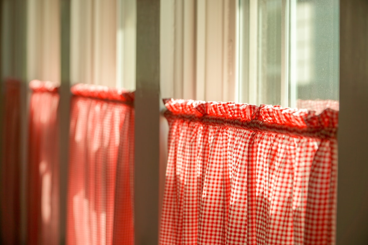 Morning sunlight shining through vintage kitchen windows of an old farm house with classic southern red checkered curtains. related to Kitchen Valance Patterns: Elevate Your Kitchen Decor