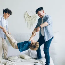 Mother father swinging child holding hands and feet then putting on bed at home related to Transform Your Home with Family Dollar Bedding: Affordable Comfort for Every Room