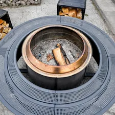 Nordic Coziness: A modern circular outdoor fire pit with stacked firewood at Iglupark in the Noblessner district of Tallinn, Estonia. related to Choosing the Perfect Patio Heater: Cast Iron or Clay Chiminea?