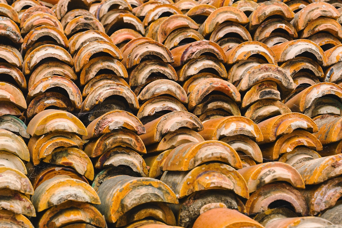 Old clay roof tiles stacked in rows showing weathered textures and colors in a rustic setting - Rows of weathered clay roof tiles create a textured pattern, showcasing various shades of orange and brown under natural light, hinting at their age and history. related to The Rustic Charm of Clay Chimineas: Fueling Gatherings and Memories