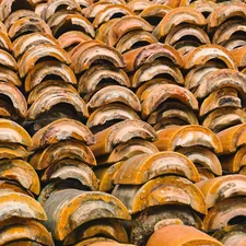 Old clay roof tiles stacked in rows showing weathered textures and colors in a rustic setting - Rows of weathered clay roof tiles create a textured pattern, showcasing various shades of orange and brown under natural light, hinting at their age and history. related to The Rustic Charm of Clay Chimineas: Fueling Gatherings and Memories