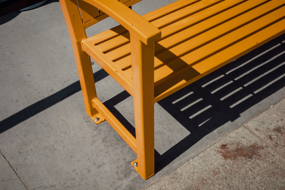 Orange wooden bench casting a shadow on pavement related to Crafting the Perfect Entryway Bench: A Comprehensive Guide to Woodworking Plans