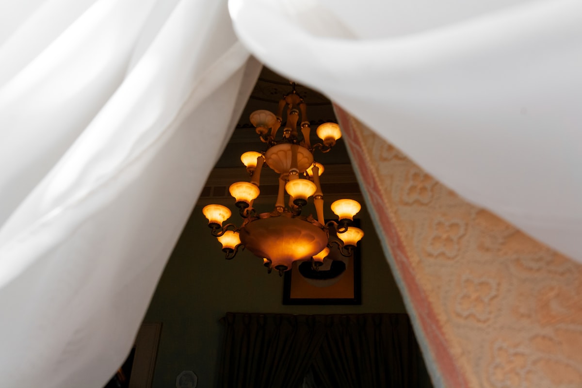 Ornate chandelier illuminated through white curtains related to Elevate Your Sleep Experience with Canopies for Beds