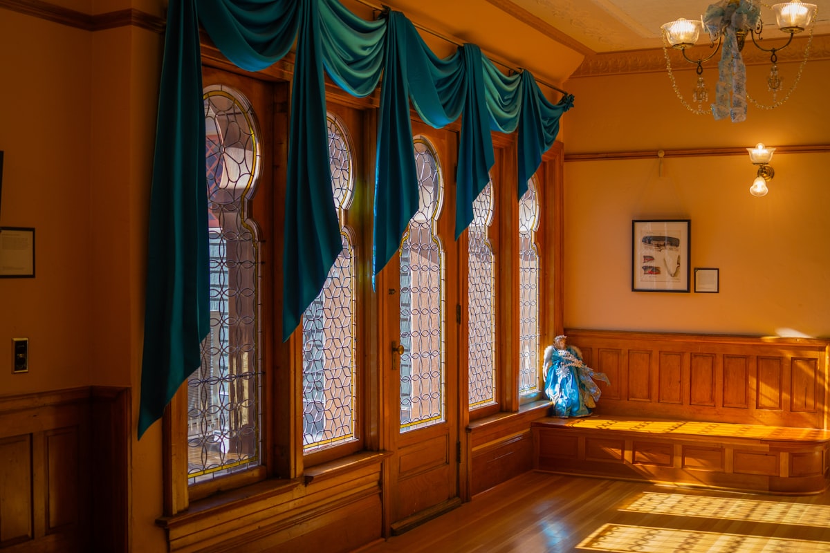 Ornate windows with teal drapes and wooden bench related to Swag Valance Curtains