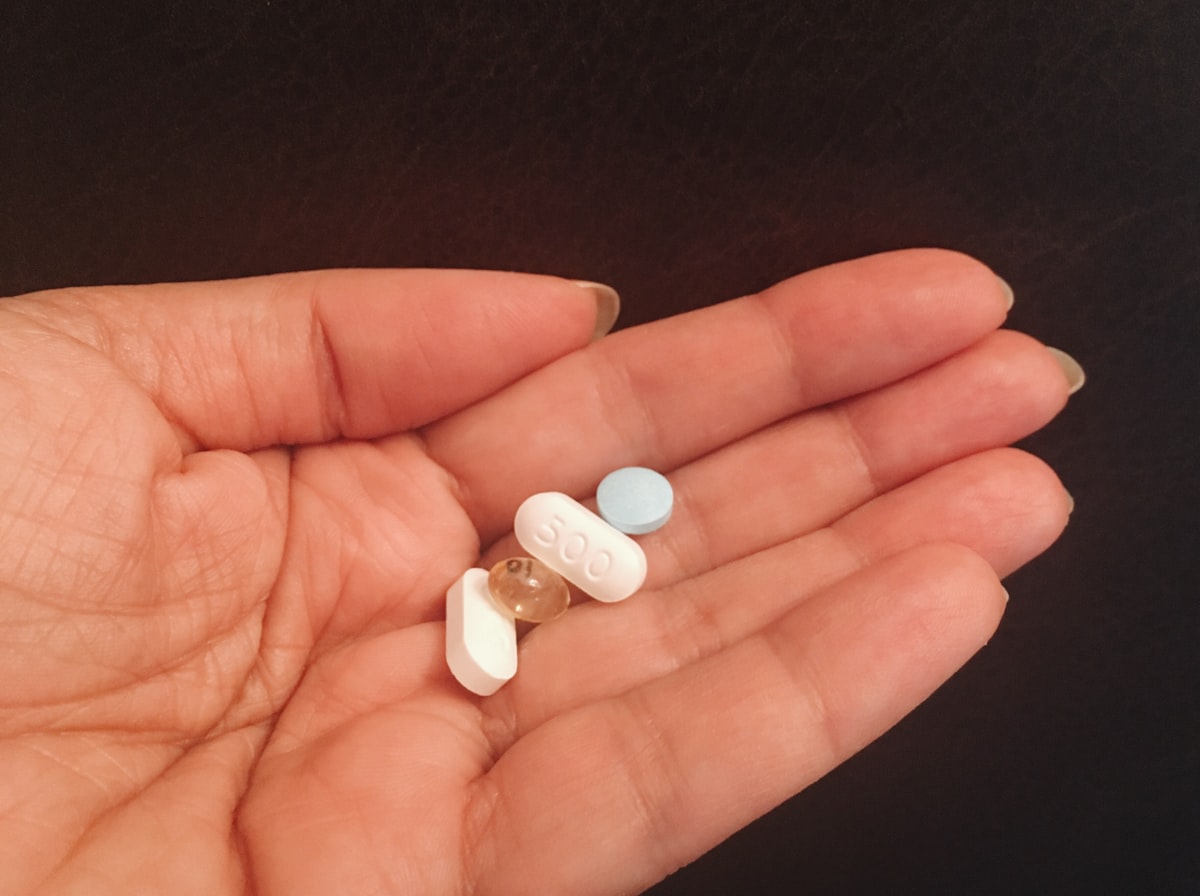 person holding four assorted medicine tablets related to Prolong Your Passion: Boosting Sexual Performance Naturally