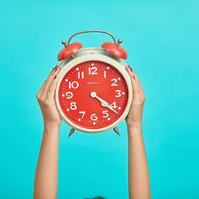 person holding red and beige twin bell analog alarm clock related to The Sweet Spot: What Time Do I Need to Go to Bed?