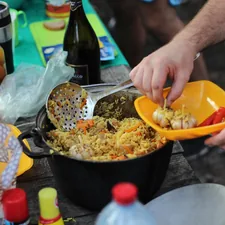 person holding yellow plastic bowl with food related to Cooking on Chiminea: A Delicious Outdoor Experience