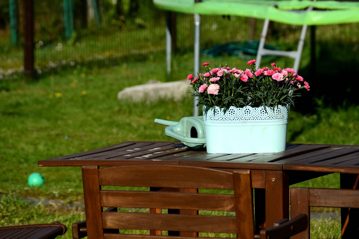 Pink flowers, watering can on wooden outdoor table. related to Transform Your Outdoor Space with Lowe's Cast Iron Chimineas