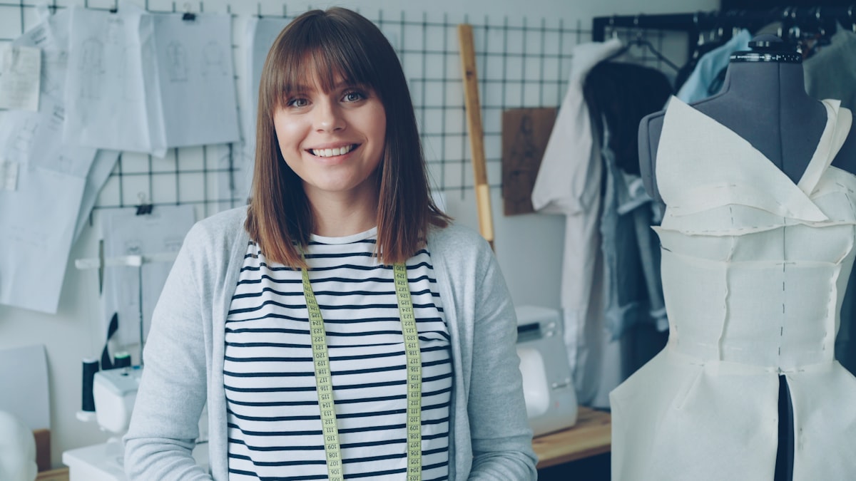 Portrait of attractive young woman clothing designer with brown hair looking at camera. Smiling confident woman is standing beside dummy, light modern tailoring workshop in background. related to Sew Your Own Style: A Beginner's Guide to Valance Making
