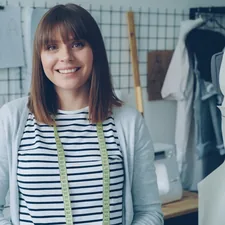 Portrait of attractive young woman clothing designer with brown hair looking at camera. Smiling confident woman is standing beside dummy, light modern tailoring workshop in background. related to Sew Your Own Style: A Beginner's Guide to Valance Making