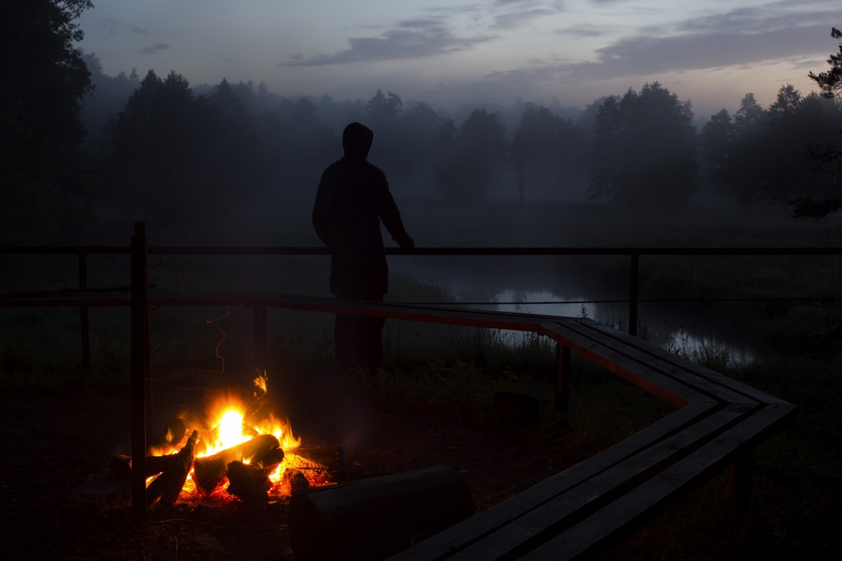 silhouette photo of a person standing near body of water and bonfire related to Cozying Up with an Outdoor Fire Chiminea