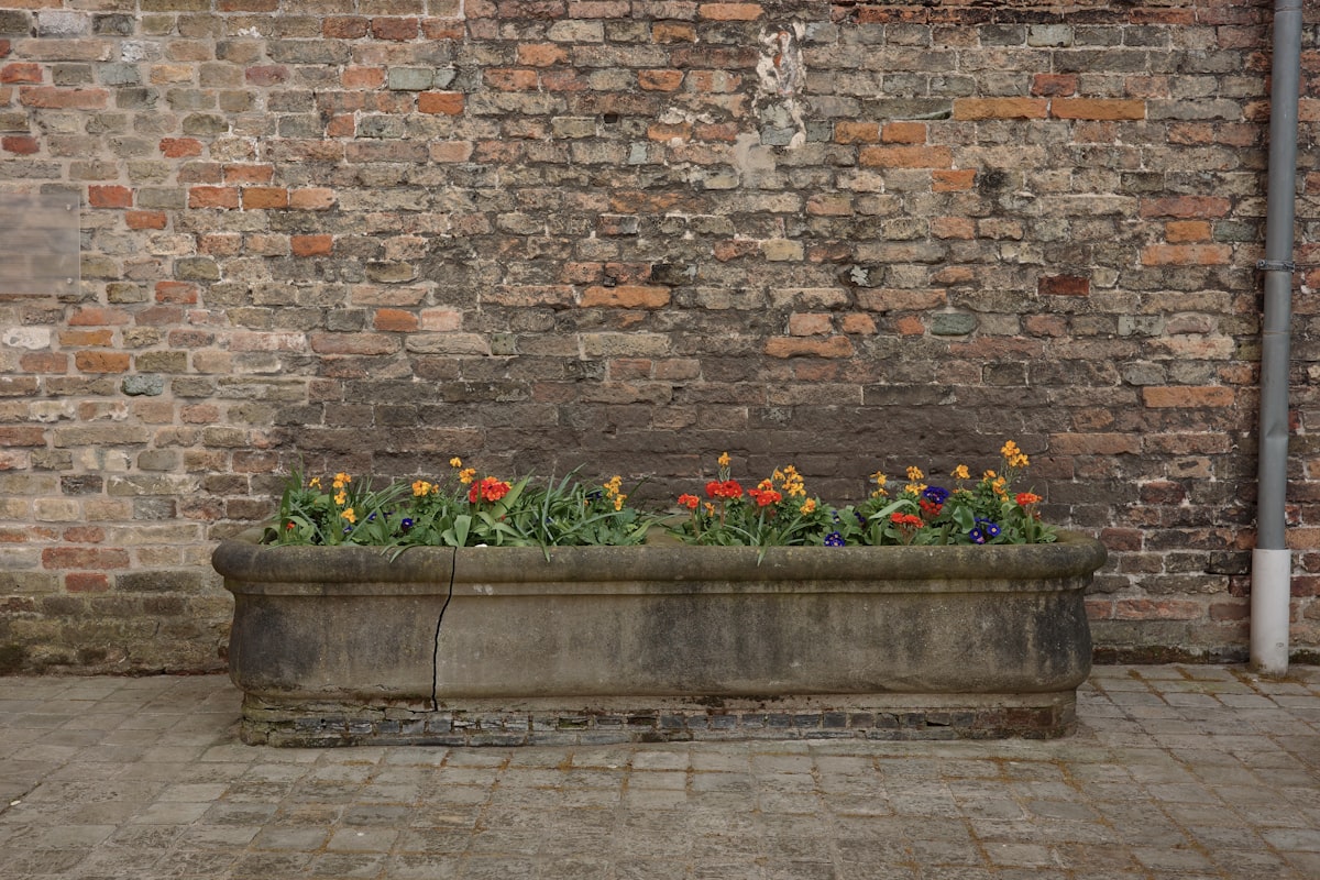 Stone planter with flowers placed against an old brick wall. Rustic urban detail, gardening, textures, outdoor decor, European courtyard aesthetic. related to Unlocking the Potential of Raised Flower Bed Kits