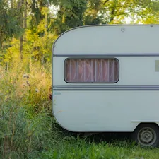 This image captures a vintage caravan resting peacefully in a lush, green woodland clearing. The soft afternoon light filters through the trees, casting a warm glow on the weathered exterior of the camper. The scene evokes a sense of quiet adventure and nostalgic tranquility, perfect for themes of travel, escape, and the simple beauty of nature. related to Cozy Up on the Open Road: The Ultimate Guide to Travel Trailer Bedding