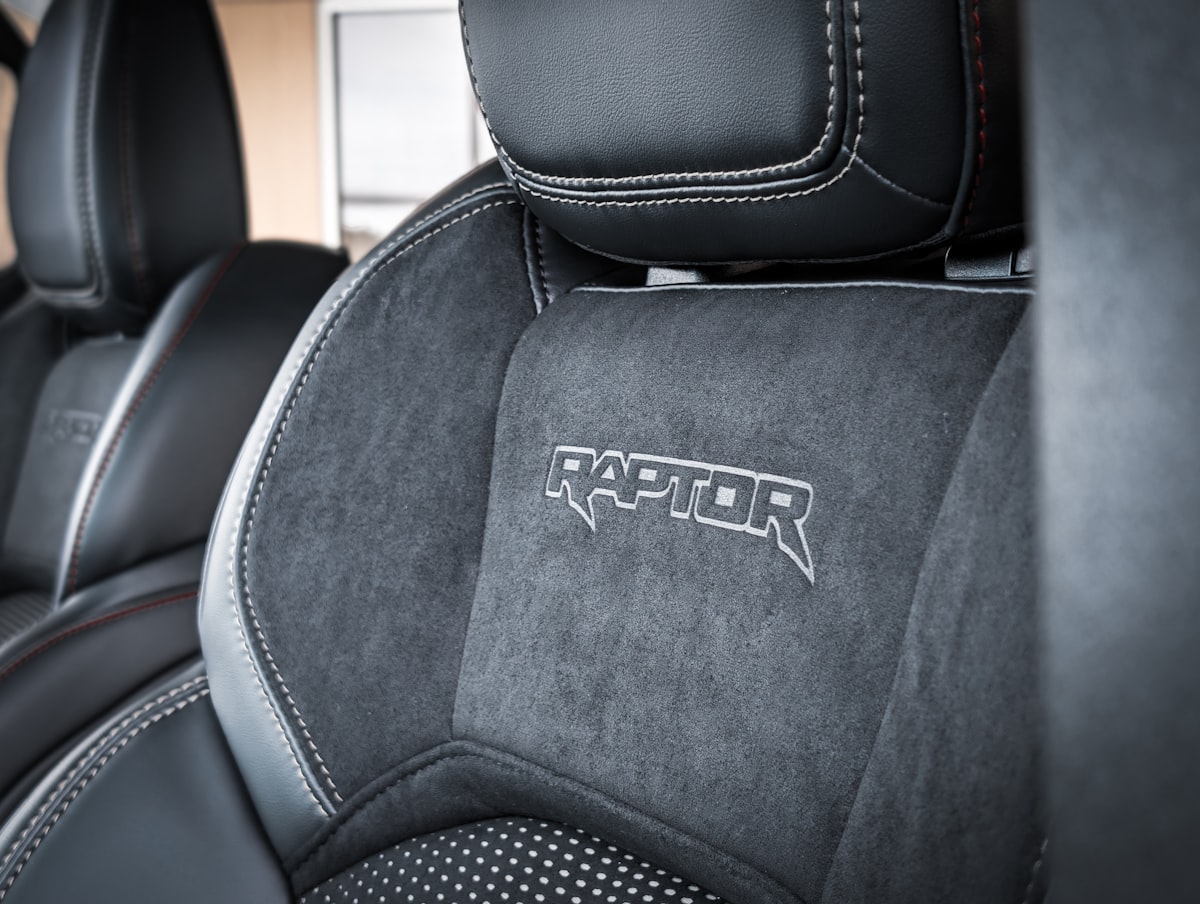 This sensational close-up captures the apex of off-road performance luxury, focusing on the meticulously crafted Raptor performance seat. The bold, embroidered logo of the sub-brand announces its lineage, set against the rich, tactile contrast of smooth leather bolsters and the technical grip of the suede-like insert. The striking white contrast stitching further emphasizes the seat's aggressive contours and premium engineering, promising intense comfort under extreme driving conditions. Boulevard Ford in Millsboro related to Ultimate Guide to Protecting Your Truck Bed