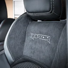 This sensational close-up captures the apex of off-road performance luxury, focusing on the meticulously crafted Raptor performance seat. The bold, embroidered logo of the sub-brand announces its lineage, set against the rich, tactile contrast of smooth leather bolsters and the technical grip of the suede-like insert. The striking white contrast stitching further emphasizes the seat's aggressive contours and premium engineering, promising intense comfort under extreme driving conditions. Boulevard Ford in Millsboro related to Ultimate Guide to Protecting Your Truck Bed