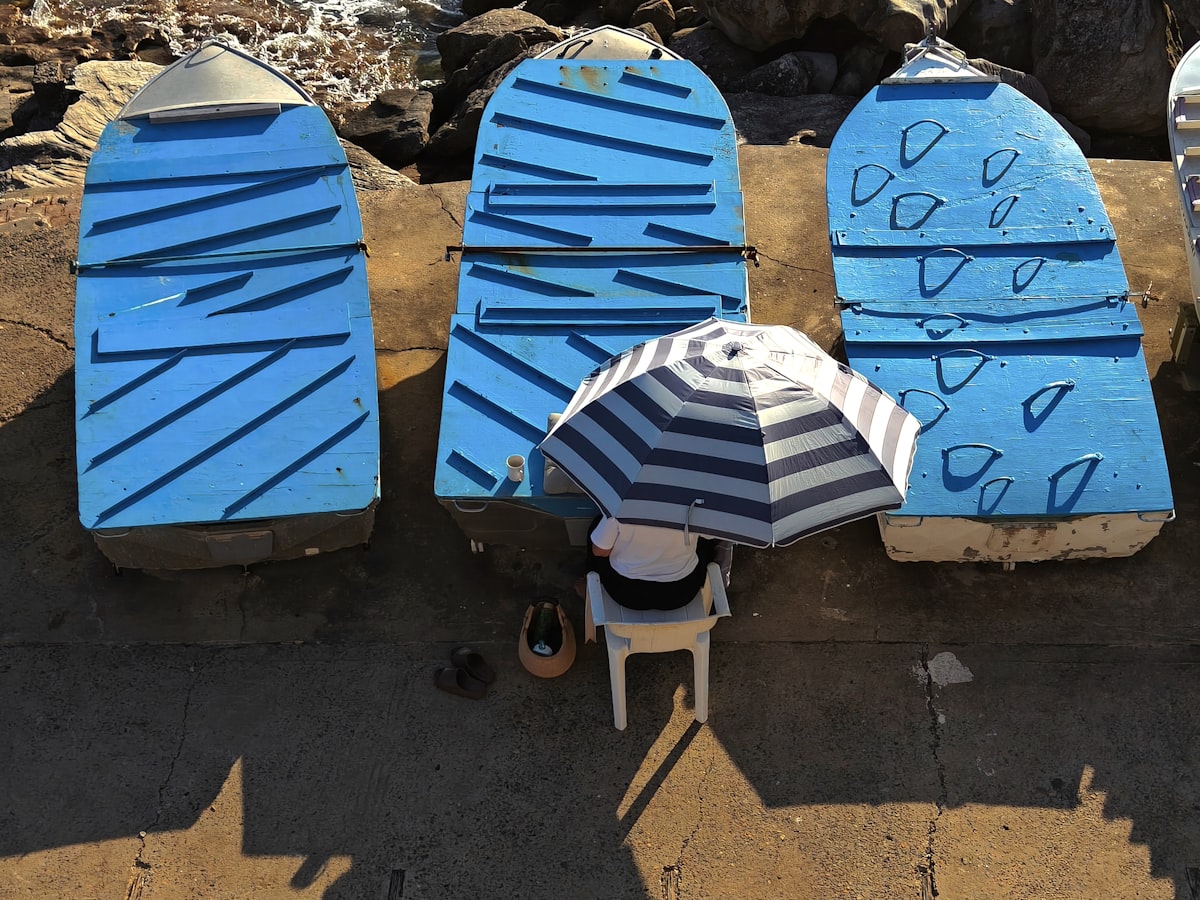 Three blue surfboards with a person under an umbrella related to Tanning in the Past: The Lowdown on Used Tanning Beds