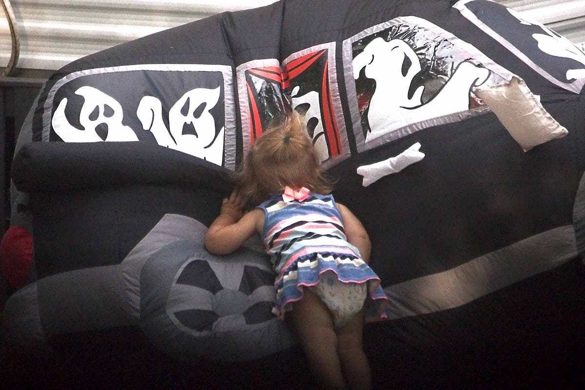 Toddler peeking into a halloween inflatable decoration. related to The Magic of Black Toddler Bed: A Guide to Styling Your Child's Dreams