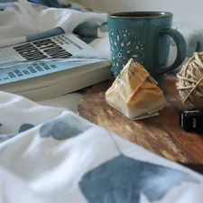 Turkish coffee on a wooden tray and a book on the bed.  related to Weaving Whimsy: A Guide to Magical Thinking Bedding