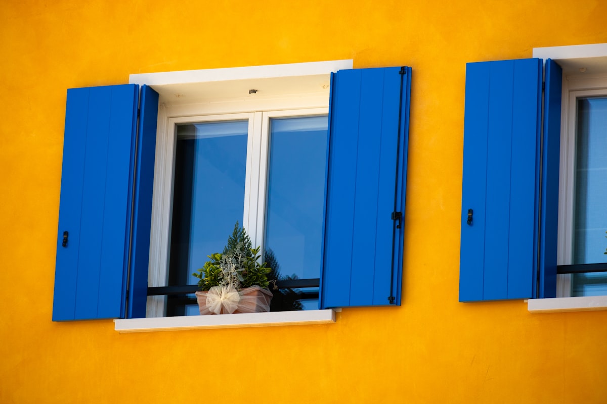two windows with blue shutters and a potted plant related to Solid Color Valances for Windows