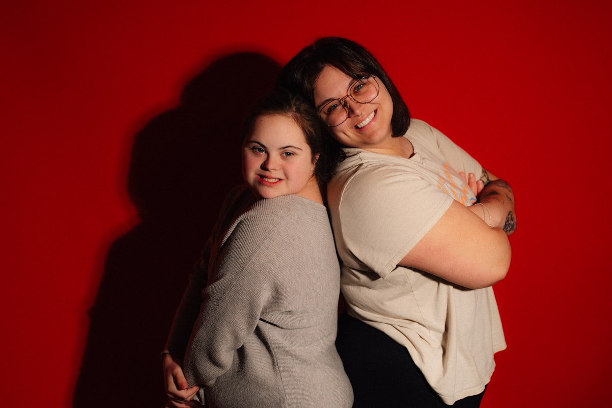 Two women smiling back to back on red background related to The Ultimate Guide to Twin Bed Sizes: How Big is a Twin Bed?