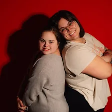 Two women smiling back to back on red background related to The Ultimate Guide to Twin Bed Sizes: How Big is a Twin Bed?