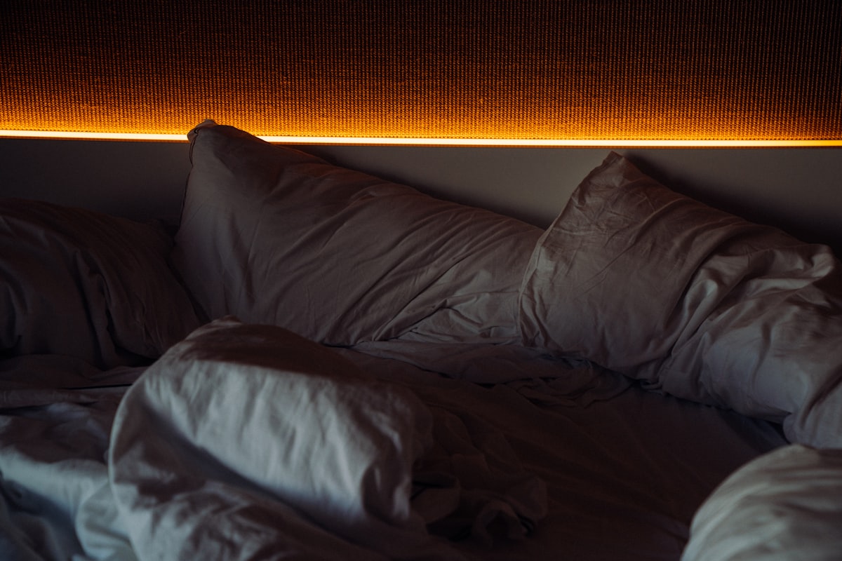 Unmade bed with warm ambient lighting above related to The Enchanting World of Lights Around Bed