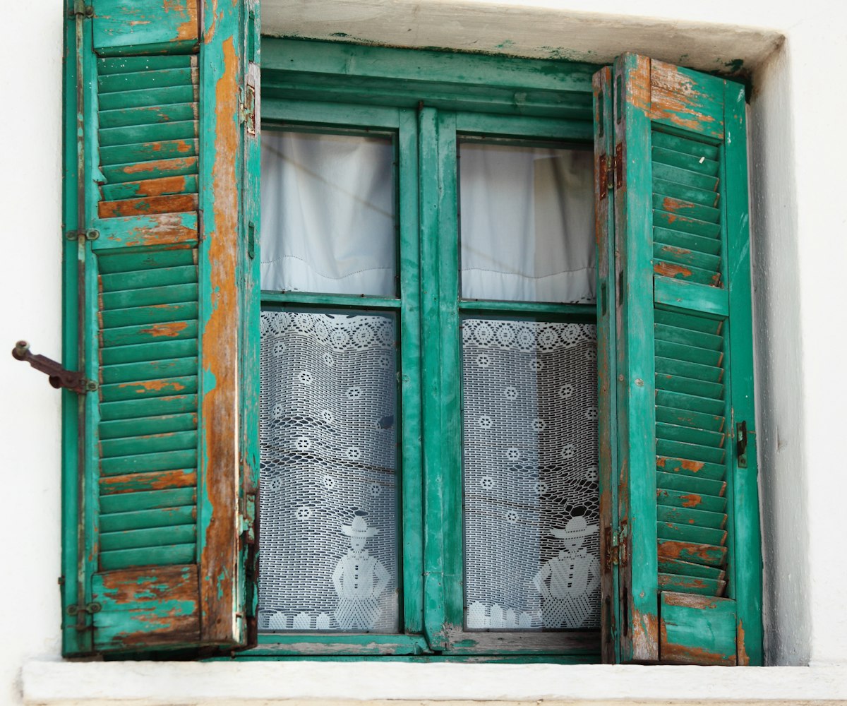 Village home window with embroidered curtains and flaked paint on the shutters. related to Incorporating Teal Window Valances into Your Home Decor