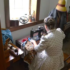 Volunteer at Historical farm sewing on treadle sewing machine related to Making a Valance
