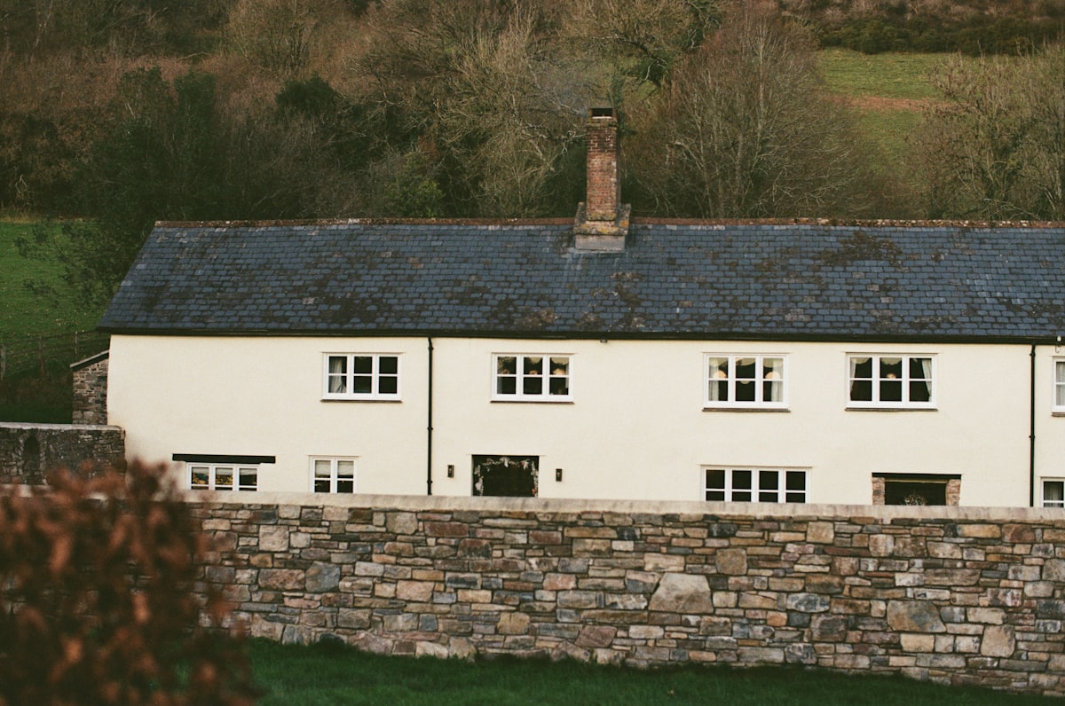 White cottage with stone wall in front related to Embrace Rustic Charm: The Allure of Stone Cottage Bedding