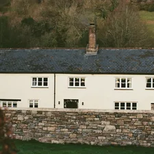 White cottage with stone wall in front related to Embrace Rustic Charm: The Allure of Stone Cottage Bedding