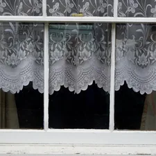 White wooden three panel window hung with scalloped white lace curtains related to Enhancing Window Décor with Valances and Swags