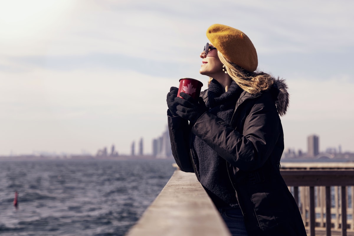 woman in black leather jacket and brown knit cap holding red ceramic mug related to Warming Up to Style: The Benefits of a Large Steel Chiminea