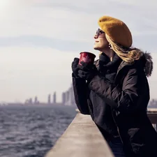 woman in black leather jacket and brown knit cap holding red ceramic mug related to Warming Up to Style: The Benefits of a Large Steel Chiminea