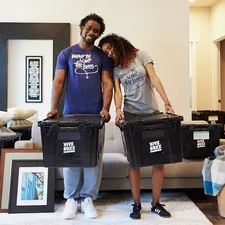 woman in blue tank top and gray leggings holding black suitcase related to Cozy Up with Style: Top Trends in Crate and Barrel Bedding