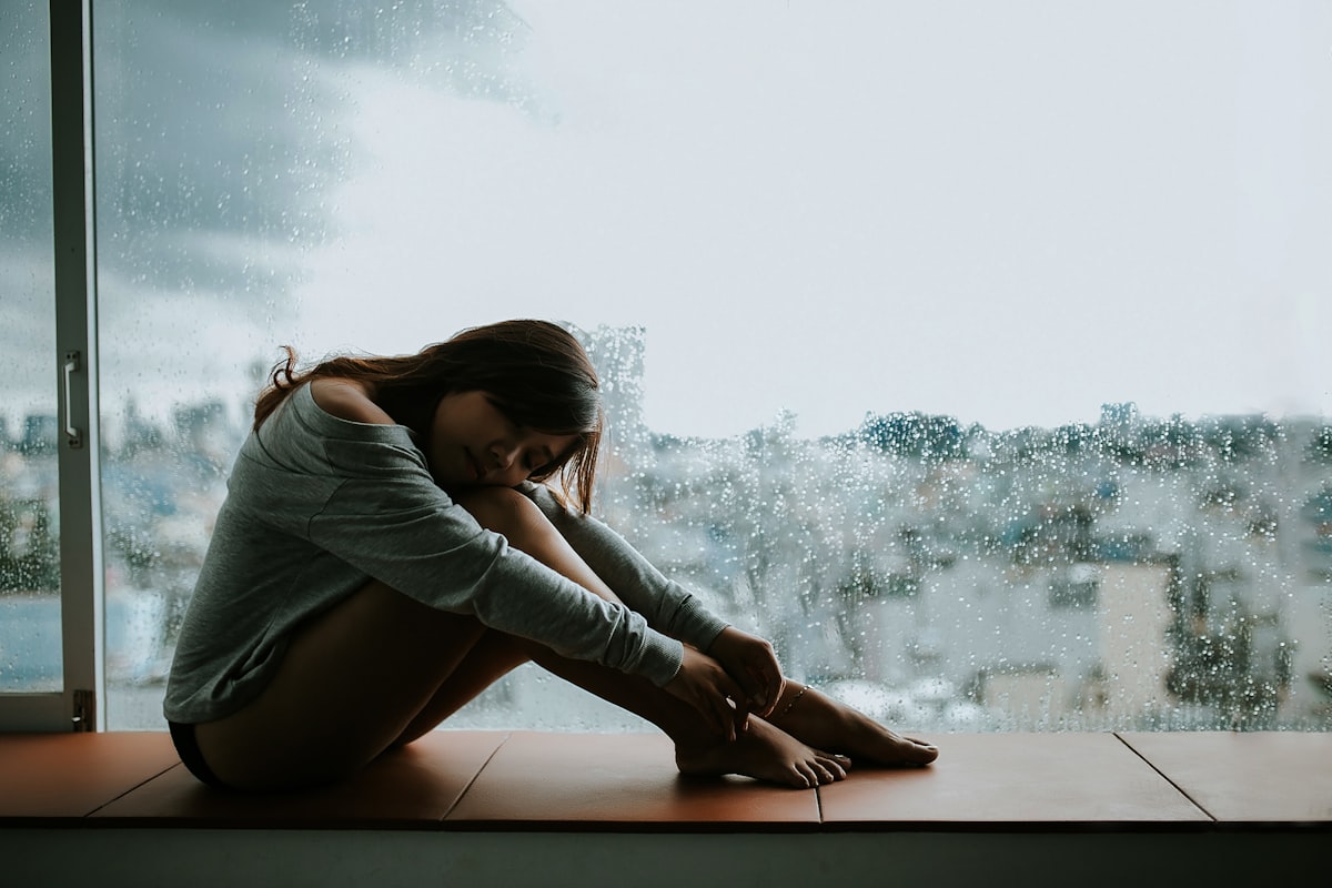 woman in gray long sleeve shirt sitting on window related to When Depression Keeps You in Bed: Understanding and Overcoming the Struggle