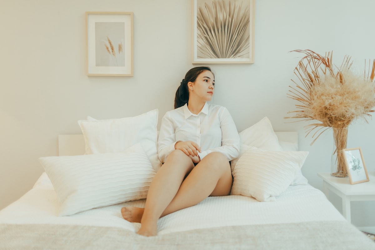 Woman in white shirt sitting on a bed. related to Say Goodbye to Back Pain: The Top Mattresses for a Restful Sleep