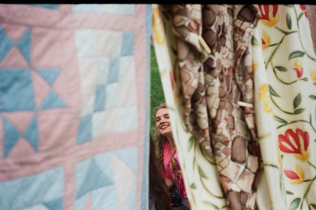 Woman peeking through colorful patterned curtains related to Cozy Comfort: Coverlets & Quilts