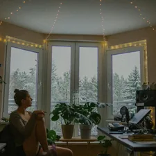Woman sitting by window with snowy trees outside related to Spruce Up Your Space with Lush Turquoise Window Valances