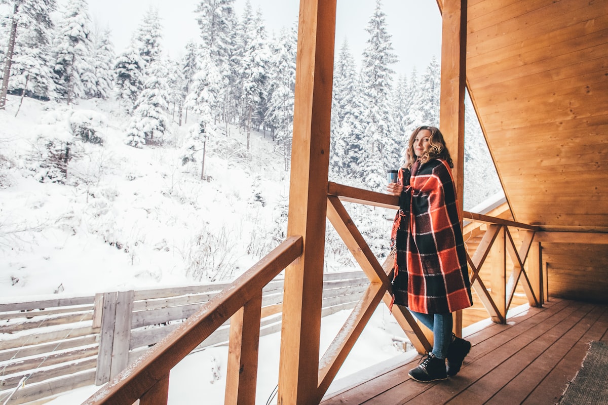 woman standing on wooden deck while wrapped with red and black blanket related to Bask in the Warmth: Choosing the Best Outdoor Chiminea for Your Yard