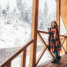 woman standing on wooden deck while wrapped with red and black blanket related to Bask in the Warmth: Choosing the Best Outdoor Chiminea for Your Yard