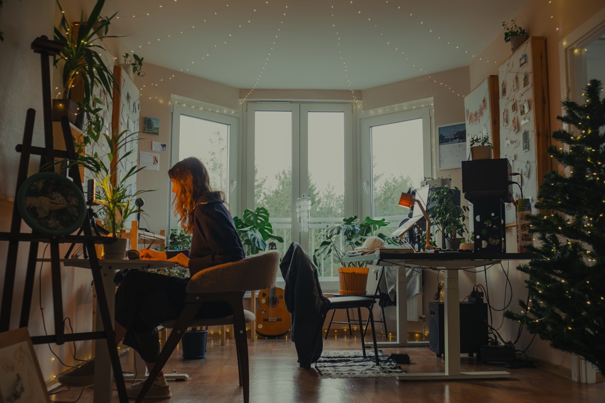 Woman working at a desk in a cozy, plant-filled room. related to Elevate Your Space with the Perfect Valance and Curtain Set