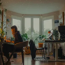 Woman working at a desk in a cozy, plant-filled room. related to Elevate Your Space with the Perfect Valance and Curtain Set