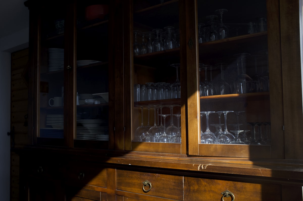 Wooden cabinet with glassware illuminated by sunlight. related to Unlocking the Elegance of Antique Mahogany Sideboards