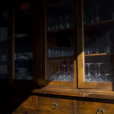 Wooden cabinet with glassware illuminated by sunlight. related to Unlocking the Elegance of Antique Mahogany Sideboards