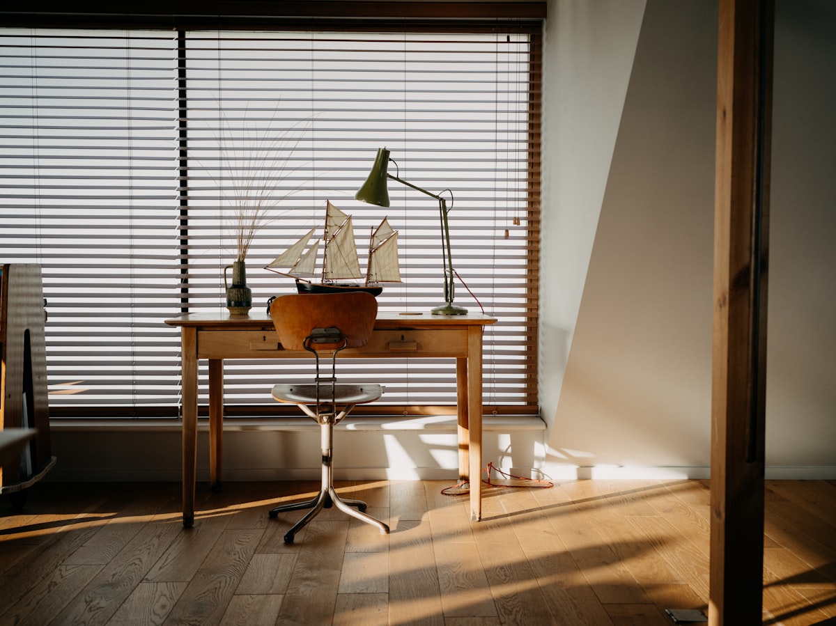 Wooden desk with model ship and lamp by window. related to Anchors Aweigh: Nautical Window Valances for a Seaside Vibe