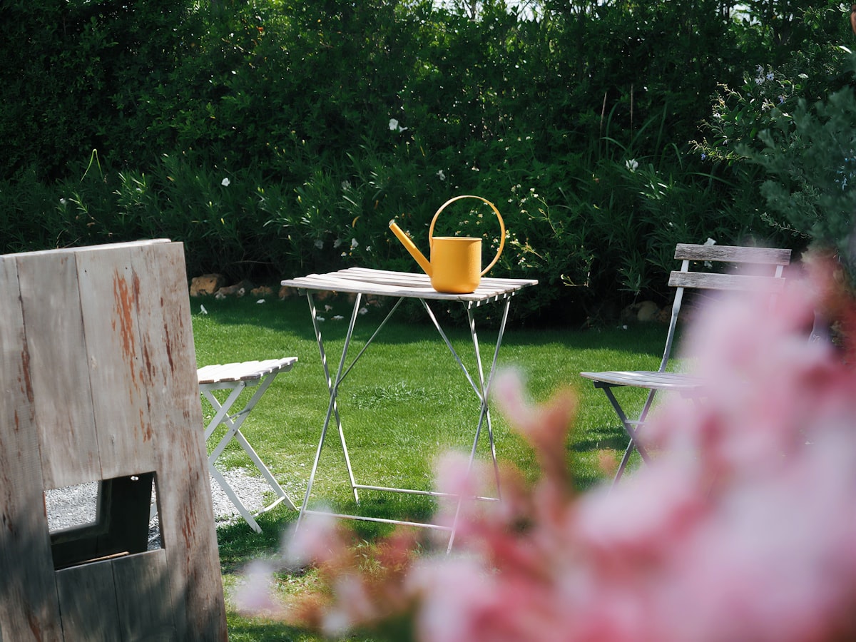 Yellow watering can on a small table in a garden. related to Transform Your Outdoor Space with a Wood Burning Chiminea: A Comprehensive Guide